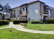 Thumbnail 12 of 26 - Apartment complex with a green lawn and a bench at The Casas Apartments, California, 92126