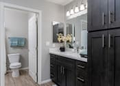 Thumbnail 18 of 26 - A bathroom with a white toilet, a sink with a mirror above it, and a cabinet with a door at The Casas Apartments, California, 92126