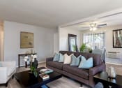Thumbnail 25 of 26 - A living room with a brown couch, a coffee table, and a painting on the wall at The Casas Apartments, San Diego, California
