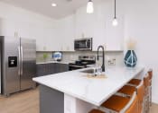 Thumbnail 12 of 59 - a kitchen with a large island with quartz countertops and stainless steel appliances at Element 12 Apartments, Henderson NV