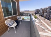 Thumbnail 30 of 59 - a balcony with two chairs and a table and a pool  in the background at Element 12 Apartments, Henderson NV