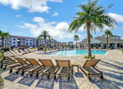 Thumbnail 3 of 30 - Outdoor pool area with lounge chairs and palm trees at The Charles apartments