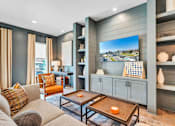 Thumbnail 18 of 30 - A resident lounge with a grey couch, a coffee table, and a large TV mounted on the wall.