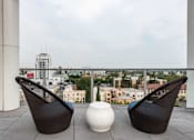 Thumbnail 31 of 34 - Two black chairs and a white vase on a balcony with a city view.