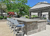 Thumbnail 16 of 30 - A patio with a bar and chairs under a pergola.