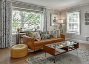 Thumbnail 26 of 30 - A living room with a brown couch, a glass coffee table, and a yellow pouf.