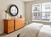 Thumbnail 9 of 22 - A bedroom with a large bed, a wooden dresser, and a round mirror on the wall.