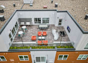 Thumbnail 42 of 61 - A patio with orange chairs and a table is surrounded by buildings.