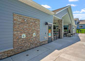 Thumbnail 20 of 76 - A building with a grey siding and a stone wall with two signs on it.