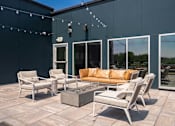 Thumbnail 19 of 32 - A patio with a couch, chairs, and a fire pit.