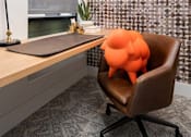 Thumbnail 26 of 43 - A chair with an orange design on it sits in front of a desk with a lamp on it.