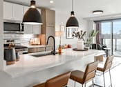 Thumbnail 5 of 43 - A modern kitchen with a white countertop and brown chairs.