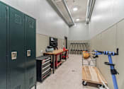 Thumbnail 38 of 50 - A workshop with green lockers, a workbench, and a cart with a bag on it.
