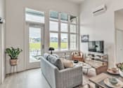 Thumbnail 6 of 50 - A modern living room with a grey couch, a coffee table with bowls and plants, and a flat-screen TV.