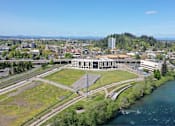 Thumbnail 46 of 50 - A large building sits in the middle of a grassy area next to a river.