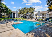 Thumbnail 14 of 26 - A large swimming pool surrounded by a stone patio and lounge chairs.