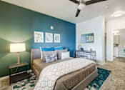 Thumbnail 10 of 33 - A bedroom with a bed, a nightstand with a lamp, a ceiling fan, and a chair.