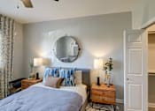 Thumbnail 11 of 33 - A bedroom with a bed, nightstands, and a round mirror on the wall.