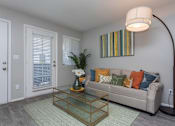 Thumbnail 9 of 20 - A living room with a glass coffee table and a striped picture on the wall.