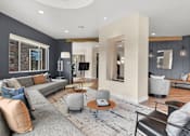 Thumbnail 17 of 30 - A modern living room with a grey sofa and a round ottoman.