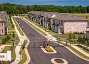 Thumbnail 7 of 26 - A street view of a residential area with houses on both sides and a gated entrance.