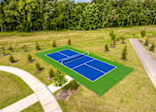 Thumbnail 5 of 26 - A blue tennis court surrounded by green grass and trees.