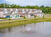 Thumbnail 18 of 26 - A fountain in the middle of a pond in front of a row of houses.