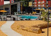 Thumbnail 31 of 34 - A large log sits in the middle of a sandy area in front of a pool.