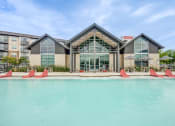 Thumbnail 1 of 26 - a swimming pool with red chairs in front of a building