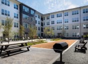 Thumbnail 18 of 26 - a courtyard with picnic tables and a barbecue grill in front of an apartment building