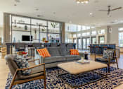 Thumbnail 10 of 29 - A residential lounge area with chairs, a center table, a grey couch, and an island countertop with barstool chairs at Parkstone at Knightdale apartments for rent in Knightdale, NC.