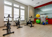 Thumbnail 16 of 29 - Three exercise bikes are lined up in a room with a red wall and a mirror.