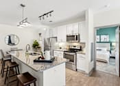 Thumbnail 1 of 29 - An interior view of a modern kitchen with a kitchen island countertop, barstool chairs, stainless steel appliances, and views of a bedroom at Parkstone at Knightdale apartments for rent in Knightdale, NC.