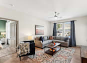 Thumbnail 3 of 29 - An interior view of a living room with a grey couch, a black chair, a coffee table, and a ceiling fan, with partial views of a bedroom at Parkstone at Knightdale apartments for rent in Knightdale, NC.