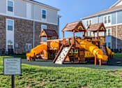 Thumbnail 18 of 29 - A playground with a yellow slide and a brown roofed structure.