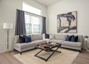 Thumbnail 9 of 26 - A living room with a grey couch, a coffee table, and a painting on the wall.