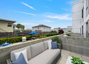 Thumbnail 55 of 58 - A modern outdoor seating area with a concrete wall and a grey couch.