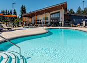 Thumbnail 18 of 34 - A swimming pool in front of a building with a person standing in the background.