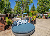 Thumbnail 26 of 34 - A blue cushioned chair with a pillow is in the foreground of a sunny courtyard.