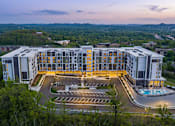 Thumbnail 4 of 28 - A large, modern building with a parking lot in front and a pool in the middle.