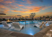 Thumbnail 1 of 28 - A pool with white chairs and a sunset in the background.