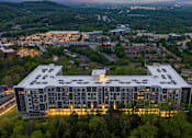 Thumbnail 6 of 28 - A large building with a lot of windows is surrounded by trees.