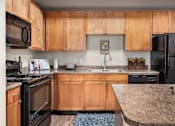Thumbnail 4 of 25 - A kitchen with wooden cabinets and black appliances.