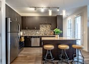 Thumbnail 1 of 26 - A kitchen with a refrigerator, a counter, and bar stools.