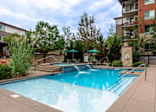 Thumbnail 9 of 26 - A swimming pool surrounded by a concrete patio and a building in the background.