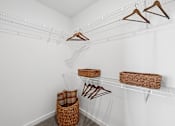 Thumbnail 25 of 28 - A white closet with clothes hanging and baskets on the shelves.