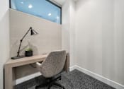 Thumbnail 41 of 41 - A grey chair is in front of a desk with a lamp and a plant on it.