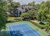 Thumbnail 17 of 39 - A tennis court surrounded by trees and a building in the background.