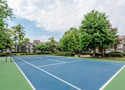 Thumbnail 15 of 39 - A blue tennis court surrounded by green trees and buildings.