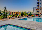 Thumbnail 21 of 24 - A swimming pool surrounded by chairs and trees with apartment buildings in the background.